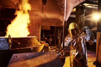 Worker holding metal rod in furnace at foundry